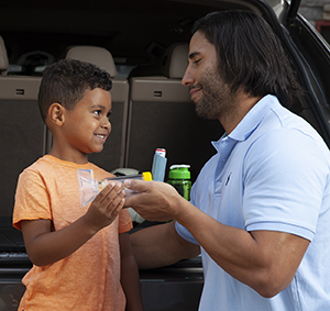 Man handing boy a metered-dose inhaler with spacer and mask.